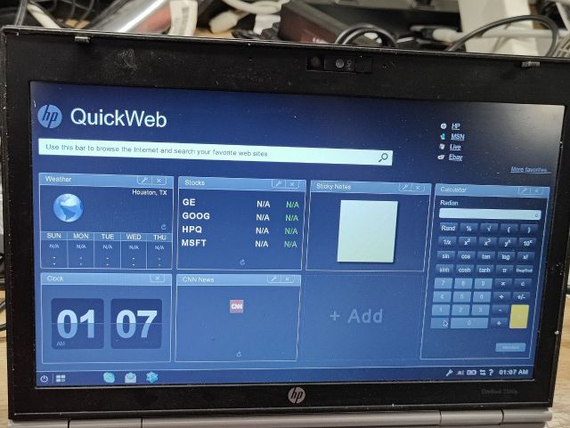 Photo of a laptop running HP QuickWeb, showing a very different widget "desktop" with CNN news headlines, sticky notes, stock ticker, clock, weather, and a calculator widget, as well as a search/address bar for launching a browser